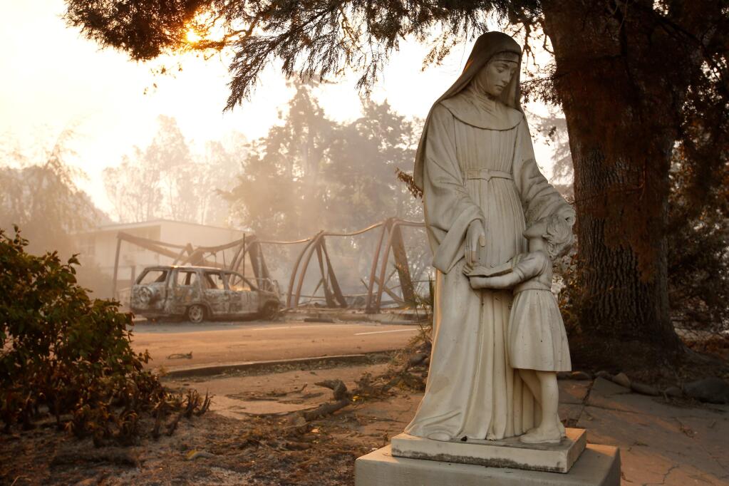 The framework of a destroyed building and burned car smolder behind a statue of Mary on the Cardinal Newman High School campus after the Tubbs Fire burned through north Santa Rosa, California on Monday, Oct. 9, 2017. (Alvin Jornada/The Press Democrat)