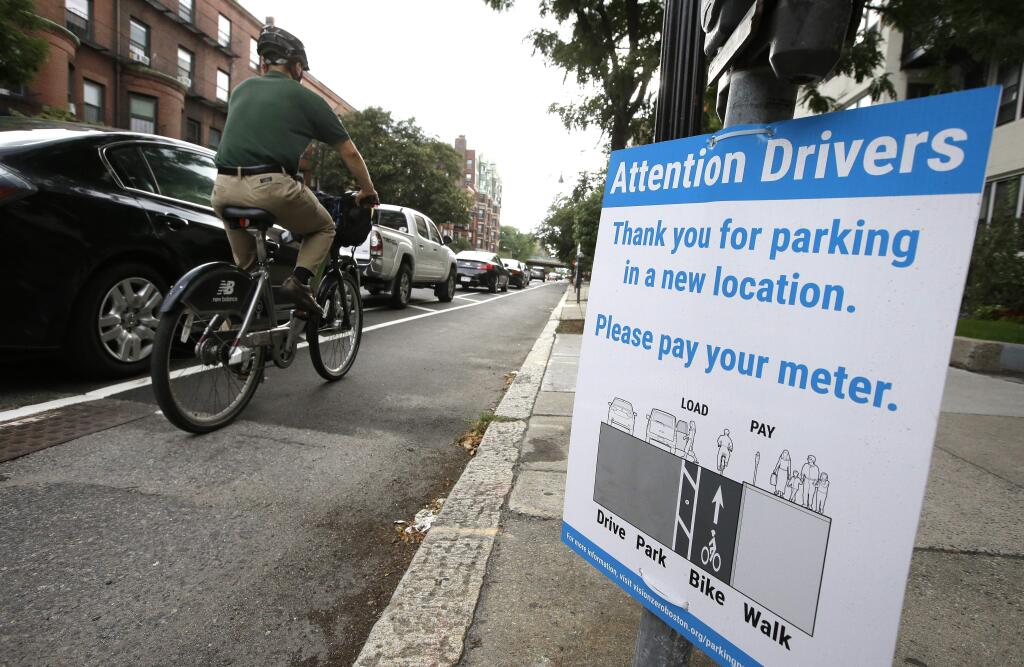 In this Tuesday, Aug. 16, 2016, photo, a cyclist rides in a bike lane between parked cars, left, and the sidewalk in Boston. Cities around the world are increasingly changing bike lanes to make them safer in light of fatal crashes involving cyclists and cars. (AP Photo/Steven Senne)