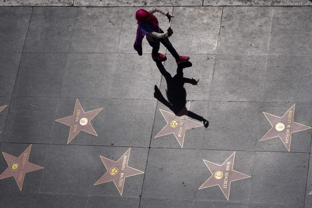 In this photo taken Wednesday, March 18, 2020, a person takes a selfie as she walks along the Walk of Fame on Hollywood Boulevard in the Hollywood section of Los Angeles. The coronavirus is hitting California's most famous tourist sites hard. From Disneyland to Yosemite National Park, the Golden State's iconic destinations are closed or shuttering amenities to prevent the spread of the pandemic. (AP Photo/Mark J. Terrill)