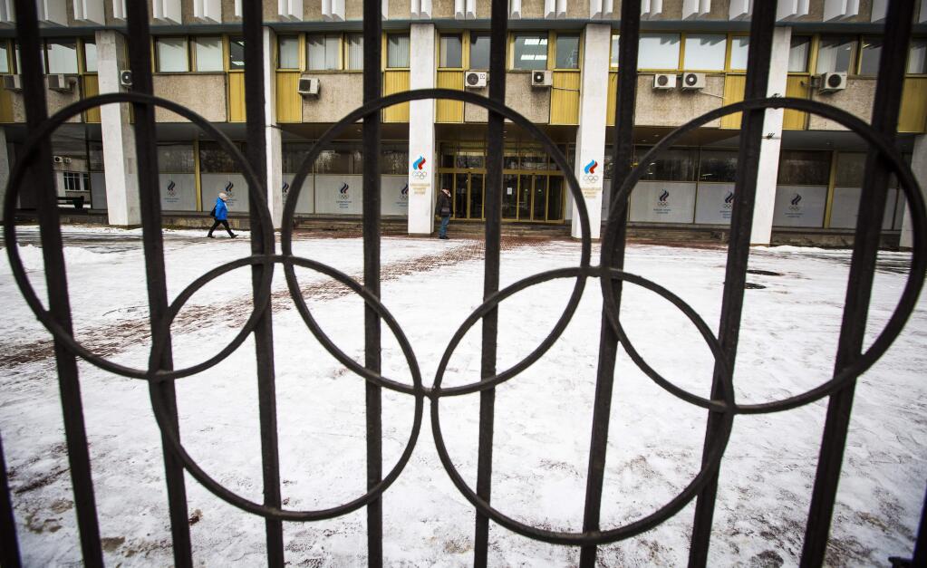 People walk at the building of the Russian Olympic Committee is seen through a gate decorated with the Olympic rings in Moscow, Russia, Wednesday, Dec. 6, 2017. The International Olympic Committee has barred the Russian team from competing in Pyeongchang in February over widespread doping at the last edition of the Winter Games in 2014. (AP Photo/Alexander Zemlianichenko)