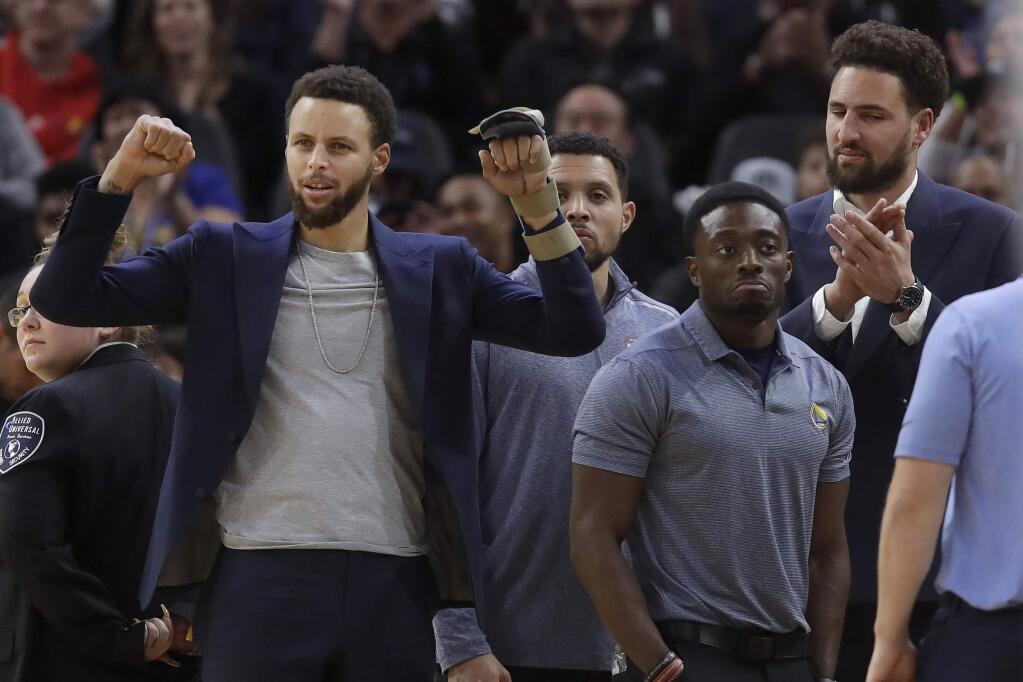 Injured Golden State Warriors guards Stephen Curry, left, and Klay Thompson, right, cheer a performer during a timeout in the second half of the team's NBA basketball game against the Chicago Bulls in San Francisco, Wednesday, Nov. 27, 2019. (AP Photo/Jeff Chiu)