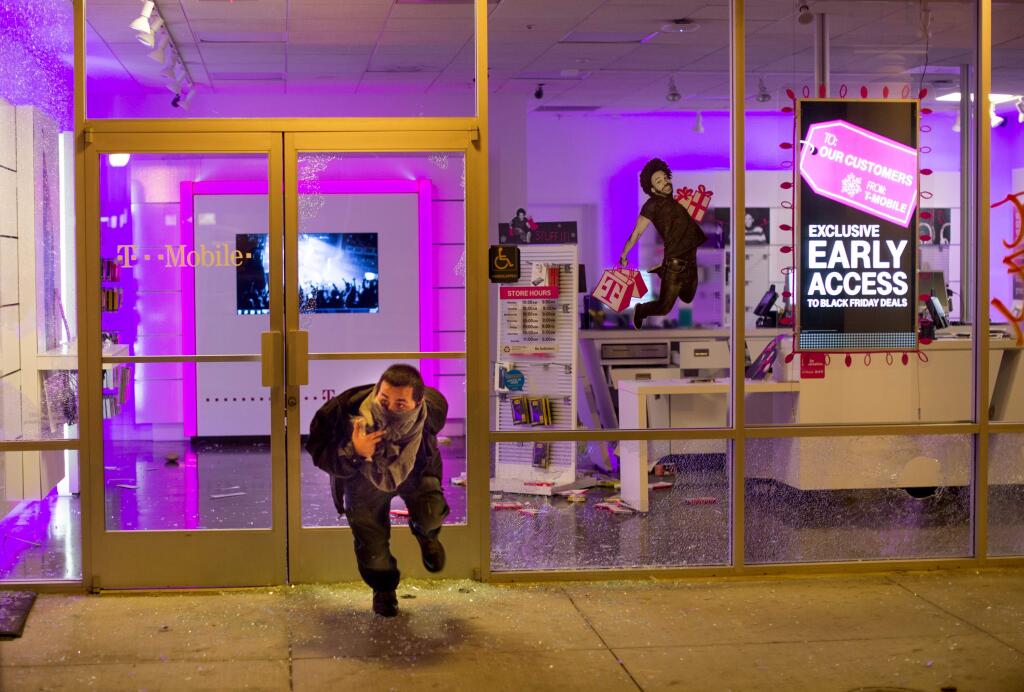 A man leaves a looted T-Mobile store in Oakland, Calif., on Tuesday, Nov. 25, 2014, a day after the announcement that a grand jury decided not to indict Ferguson police officer Darren Wilson in the fatal shooting of Michael Brown. Protesters briefly shut down two major freeways, vandalized police cars and looted businesses in downtown Oakland, smashing windows at cellphone stores, car dealerships, restaurants and convenience stores on a second night of protests. (AP Photo/Noah Berger)