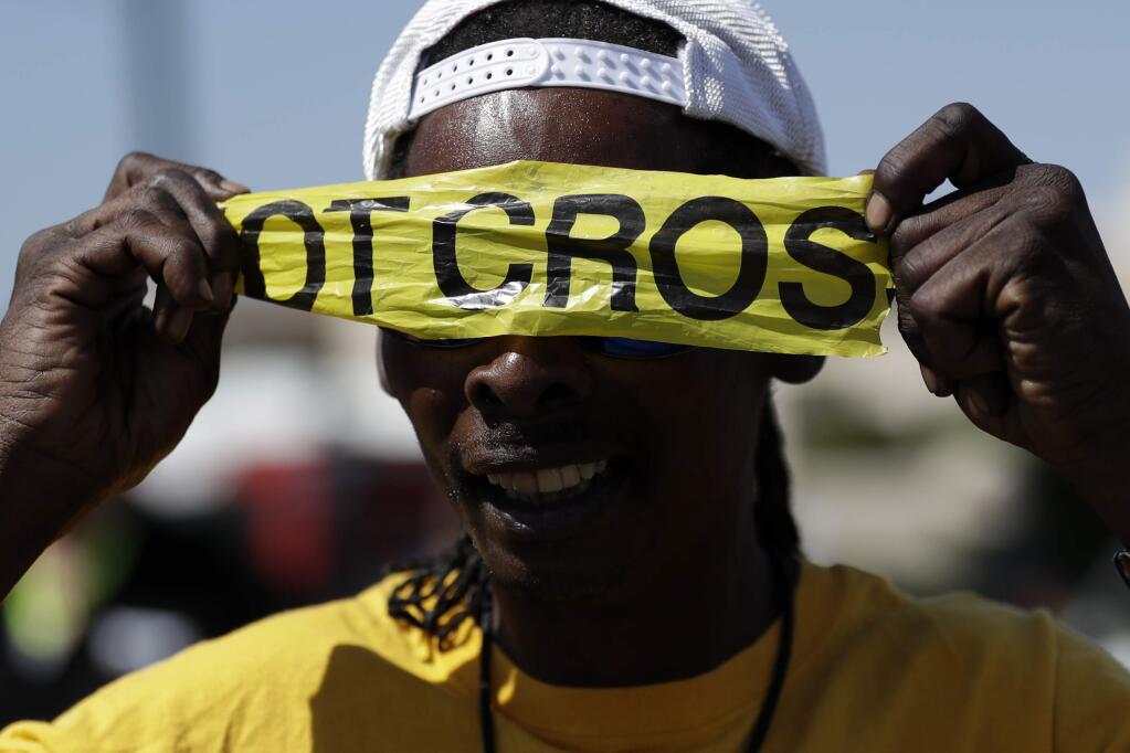 A man covers his eyes with police tape during a protest, Wednesday, Sept. 28, 2016, in El Cajon, Calif. Dozens of demonstrators on Wednesday protested the killing of a black man shot by an officer after authorities said the man pulled an object from a pocket, pointed it and assumed a 'shooting stance.' (AP Photo/Gregory Bull)
