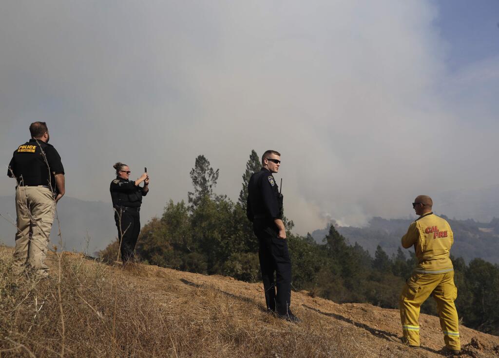Firefighters and police officers view a burning wildfire, Sunday, Oct. 15, 2017, in Oakville, Calif. With the winds dying down, fire officials in California say they are finally getting the upper hand against the wildfires that have devastated wine country and other parts of the state over the past week. (AP Photo/Marcio Jose Sanchez)
