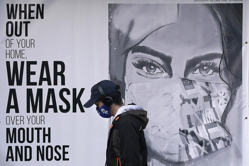 FILE - In this Saturday, Nov. 21, 2020, photo, a pedestrian wearing a mask walks past a mural during the coronavirus outbreak in San Francisco. Eleven San Francisco Bay Area counties will lift their mask requirements for vaccinated people in most indoor public settings beginning Feb. 16, 2022, when the state ends its indoor masking requirement for vaccinated people, officials announced Tuesday, Feb. 8. (AP Photo/Jeff Chiu, File)