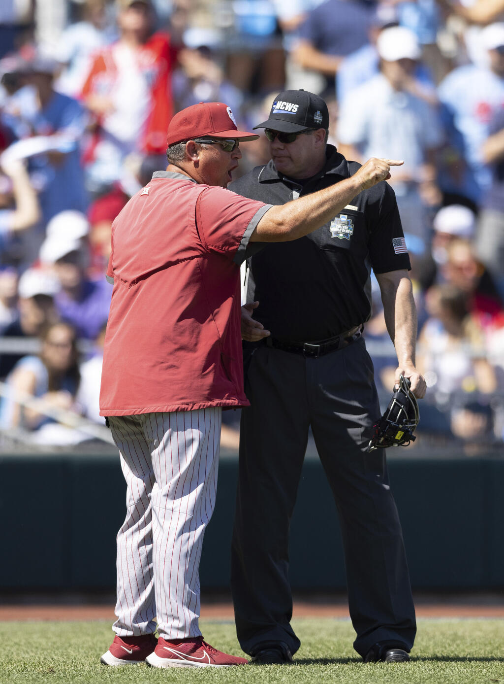 Oklahoma head coach Skip Johnson, left, argues with the umpire after a run was taken back due to interference against Mississippi by an Oklahoma first base runner in the sixth inning in Game 2 of the NCAA College World Series baseball finals, Sunday, June 26, 2022, in Omaha, Neb. (AP Photo/Rebecca S. Gratz)