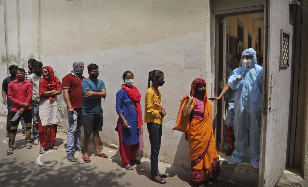A Health worker asks people to maintain the queue as they wait to give their swab samples to test for COVID-19 in New Delhi, India, April 16, 2021. The use of rapid home tests has surged in India on the back of omicron cases, which have recently begun to decline. But experts have voiced caution, saying home tests are less accurate than lab-run PCR tests and that since not all results are being reported, new variants or future clusters may go undetected. (AP Photo/Manish Swarup, File)
