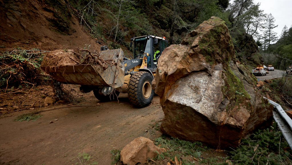Nick Taylor of Sonoma County Road Maintenance operates a front loader past a several ton boulder that fell from a hillside on Pine Flat Road, late Sunday afternoon, Jan. 8, 2023. The slide area is in the Kincade Fire zone and effectively blocked the road as crew cleared the slide near Jimtown. (Kent Porter/The Press Democrat)