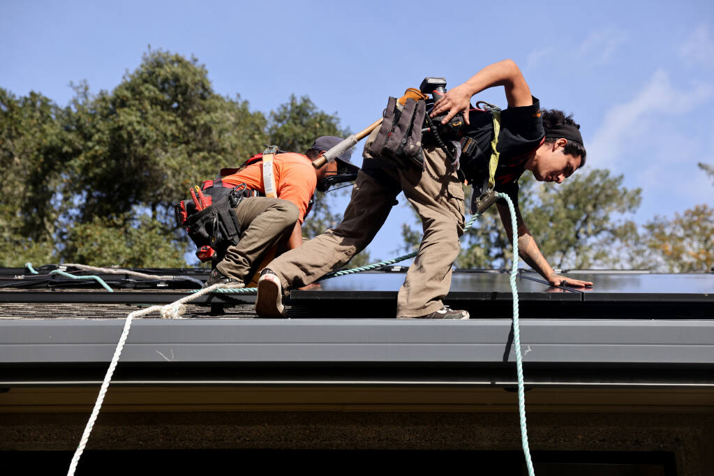 Vital Energy employees Oscar Perez-Garcia and Jose Sosa, rear, install solar panels at a home in Occidental, Calif., Monday, Nov. 28, 2022. (Beth Schlanker/The Press Democrat)