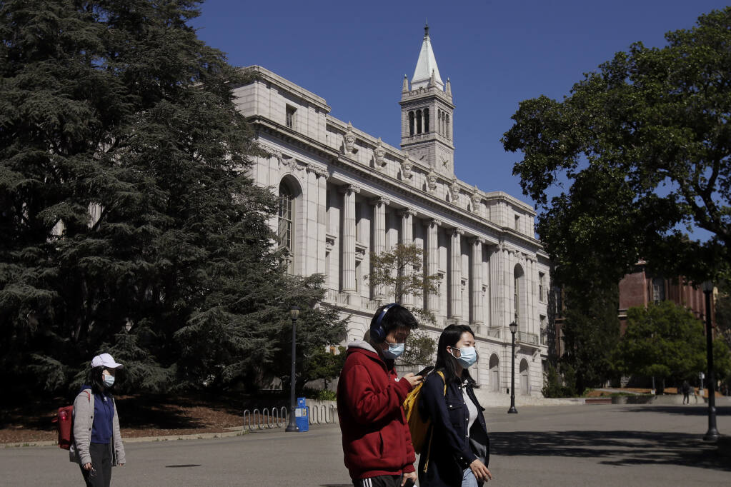 FILE - In this March 11, 2020, file photo, people wear masks while walking past Wheeler Hall on the University of California campus in Berkeley, Calif. (AP Photo/Jeff Chiu, File)