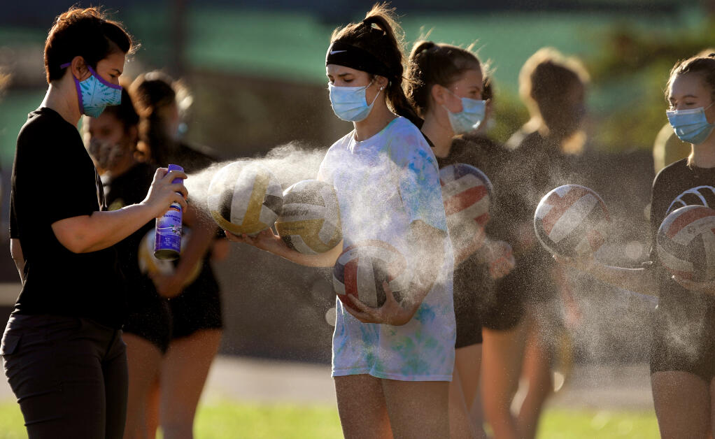 Windsor High School volleyball coach Christen Hamilton disinfects volleyballs to guard against the coronavirus, after a drill rotation, as the Jaguars hold their practice outdoors in the school quad, Wednesday, Sept. 23, 2020.   (Kent Porter / The Press Democrat) 2020