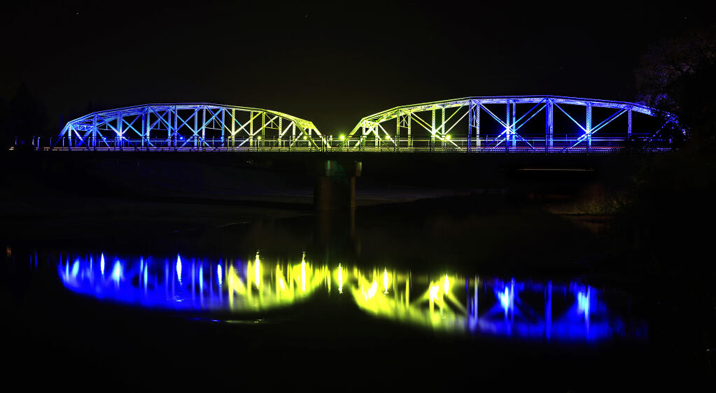 The Healdsburg Memorial Bridge is showcased in the colors of the Ukrainian flag, reflected in the Russian River, Monday, March 1, 2022, in response to the country being invaded by Russia. (Kent Porter / The Press Democrat)