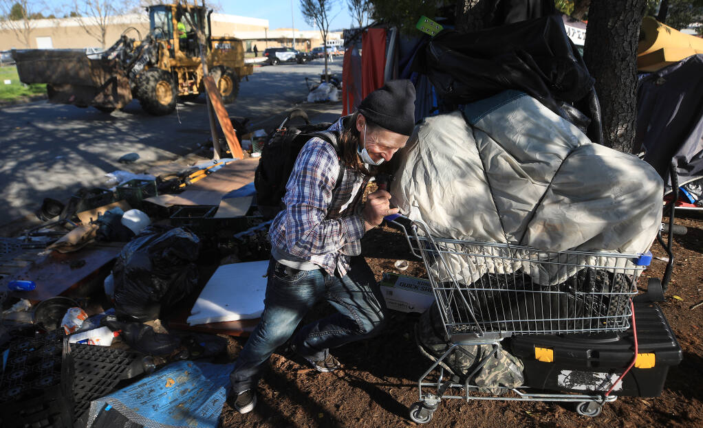 Eric Patterson struggles to move his belongings as city crews begin to clear a large homeless encampment on Industrial Drive in Santa Rosa, Tuesday, March 2, 2021. (Kent Porter / The Press Democrat) 2021
