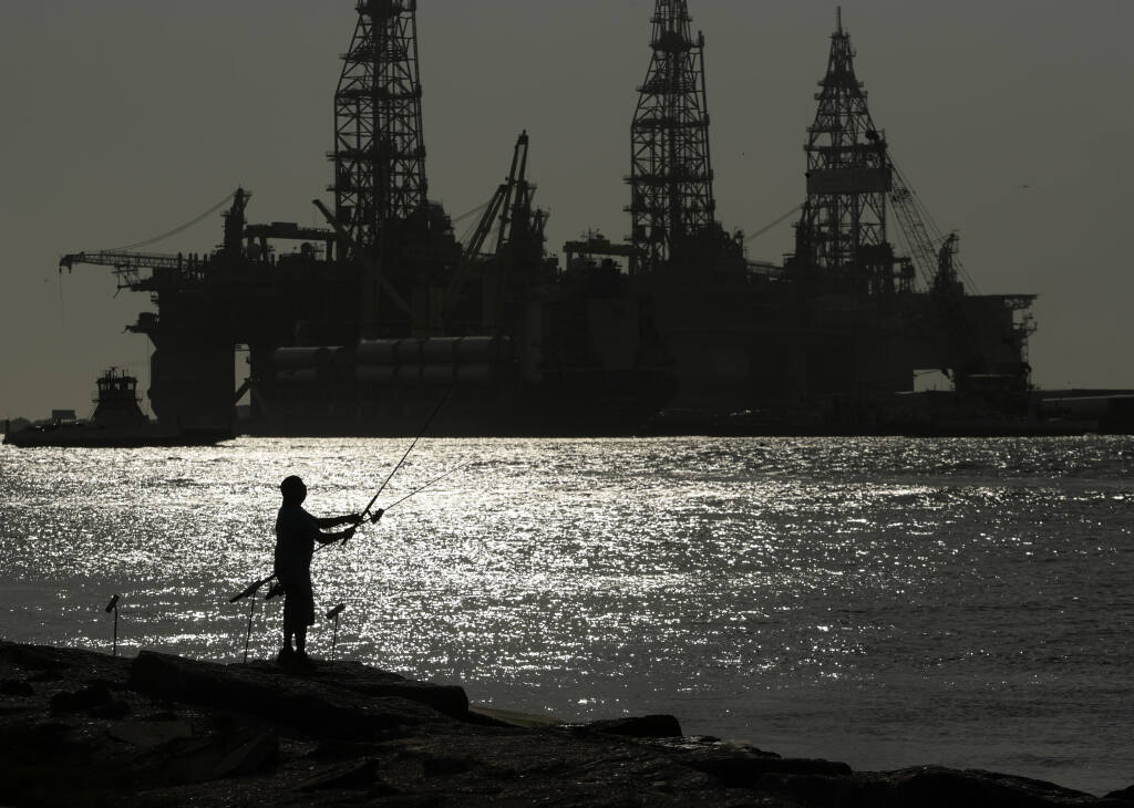 FILE - A man wears a face mark as he fishes near docked oil drilling platforms, on May 8, 2020, in Port Aransas, Texas. A federal court has rejected a proposed lease auction for offshore oil drilling in the Gulf of Mexico, saying the Biden administration failed to conduct a proper environmental review. The decision on Jan. 27, 2022, by U.S. District Judge Rudolph Contreras sends the proposed lease sale back to the Interior Department to decide next steps. (AP Photo/Eric Gay, File)