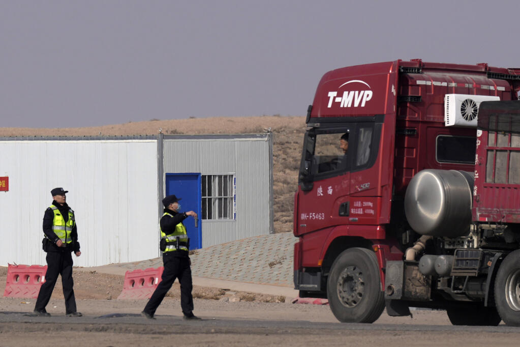 Police officers talk to a truck driver stopped at a checkpoint along a road in Qingtongxia on northern China's Ningxia Hui Autonomous Region leading to the site of a collapsed open pit mine in Alxa League in northern China's Inner Mongolia Autonomous Region, Friday, Feb. 24, 2023. Rescuers have changed their approach to search for dozens of people missing from a coal mine collapse in northern China to avoid further landslides, state broadcaster CCTV reported Friday. (AP Photo/Ng Han Guan)