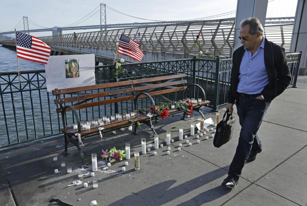 A man walks past candles, flowers, and a photo of Kate Steinle at a memorial site on Pier 14 Friday, Dec. 1, 2017, in San Francisco. In this fiercely liberal city, city leaders remained attached to San Francisco's sanctuary city status despite a not guilty verdict in a killing that sparked feverish immigration debates because the man who fired the gun was in the country illegally after being deported five times. (AP Photo/Ben Margot)