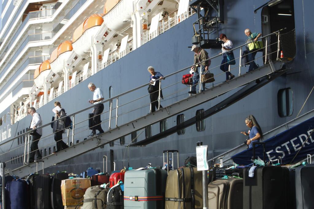Passengers of the MS Westerdam, back, owned by Holland America Line, disembark at the port of Sihanoukville, Cambodia, Saturday, Feb. 15, 2020. After being stranded at sea for two weeks because five ports refused to allow their cruise ship to dock, the passengers of the MS Westerdam were anything but sure their ordeal was finally over. (AP Photo/Heng Sinith)