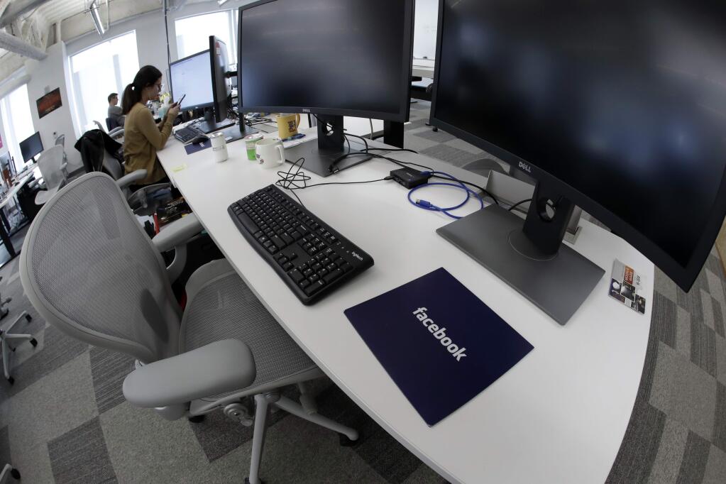 FILE- In this Jan. 9, 2019, file photo, Facebook employees sit at their stations during a tour of its new 130,000-square-foot offices in Cambridge, Mass. Facebook is raising what it pays U.S. contractors who do some of its most taxing work, including watching violent and other objectionable material for possible removal from the service. Facebook said Monday, May 13, that it will pay at least $18 an hour for these jobs. (AP Photo/Elise Amendola, File)