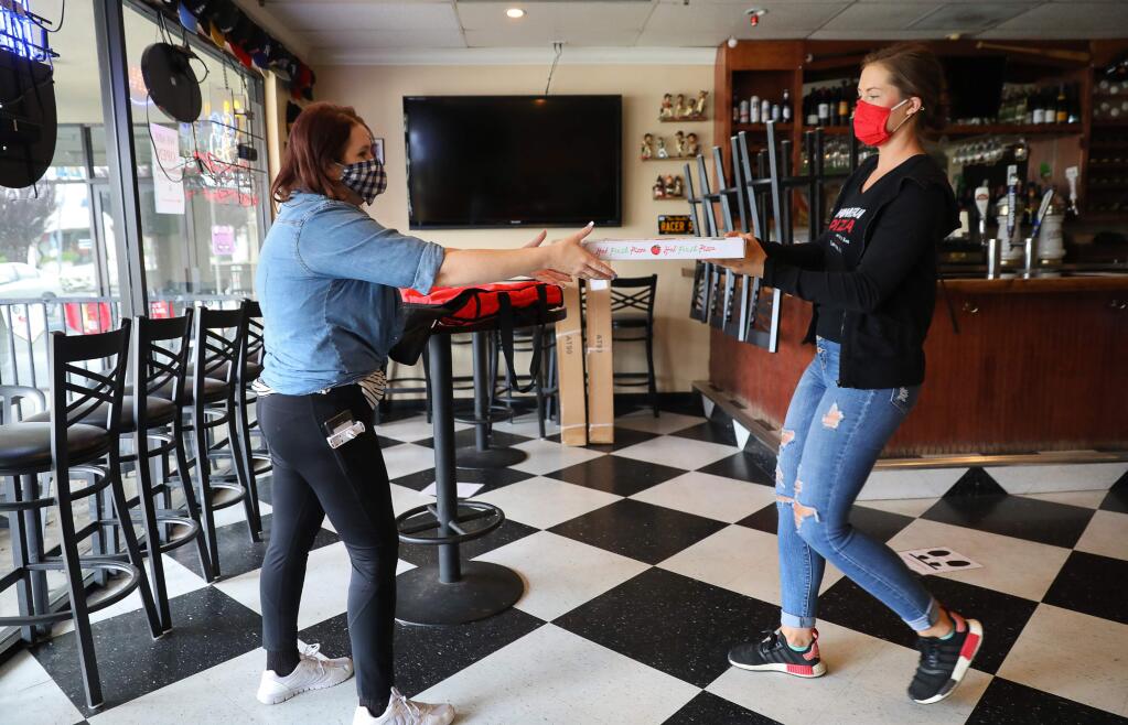 DoorDash driver Tiffany Evergrace, left, picks up a pizza for a customer from Cara Watts at Homerun Pizza & Sports Bar, in Larkfield on Thursday, May 14, 2020. (Christopher Chung/ The Press Democrat)