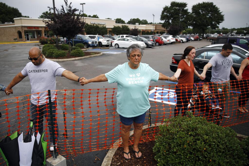 FILE - In this Saturday, June 1, 2019 file photo, Lisa Dunaway, center, of Virginia Beach, Va., holds hands with other mourners during a vigil in response to a fatal shooting at a municipal building in Virginia Beach, Va. A longtime city employee opened fire at the building Friday, killing several before police shot and killed him, authorities said. (AP Photo/Patrick Semansky)
