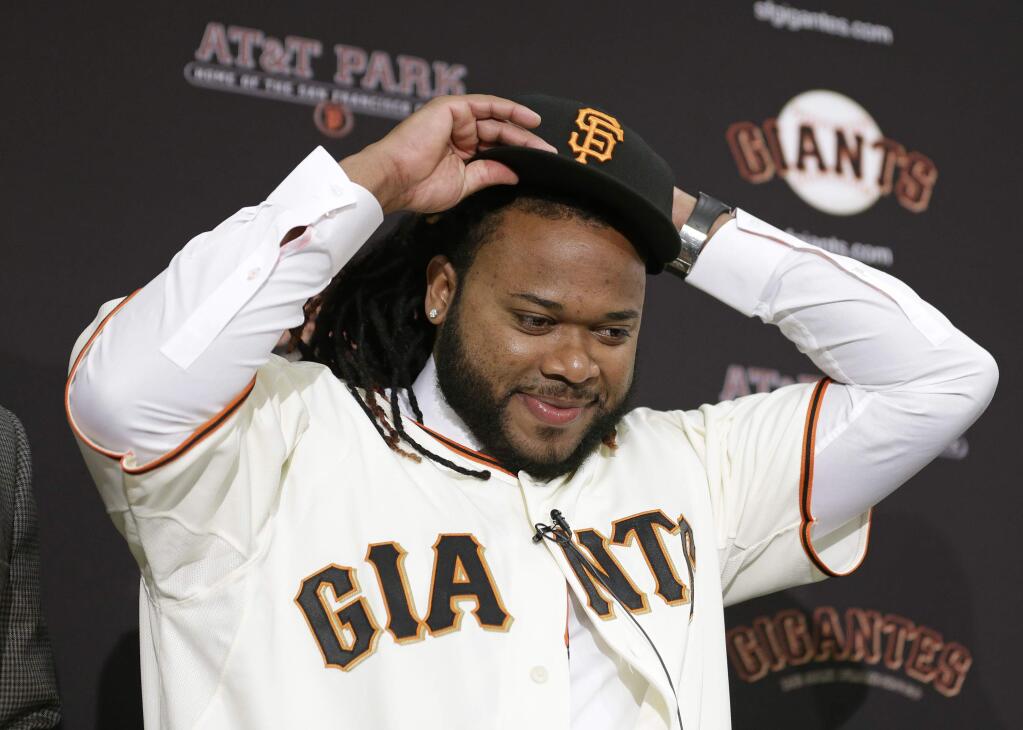 San Francisco Giants pitcher Johnny Cueto puts on a new cap during a media availability Thursday, Dec. 17, 2015, in San Francisco. Cueto was introduced by the Giants a day after passing his physical to complete a $130 million, six-year contract. Cueto, who helped the Royals win the World Series, joins a rotation led by Madison Bumgarner and new addition Jeff Samardzija. (AP Photo/Eric Risberg)