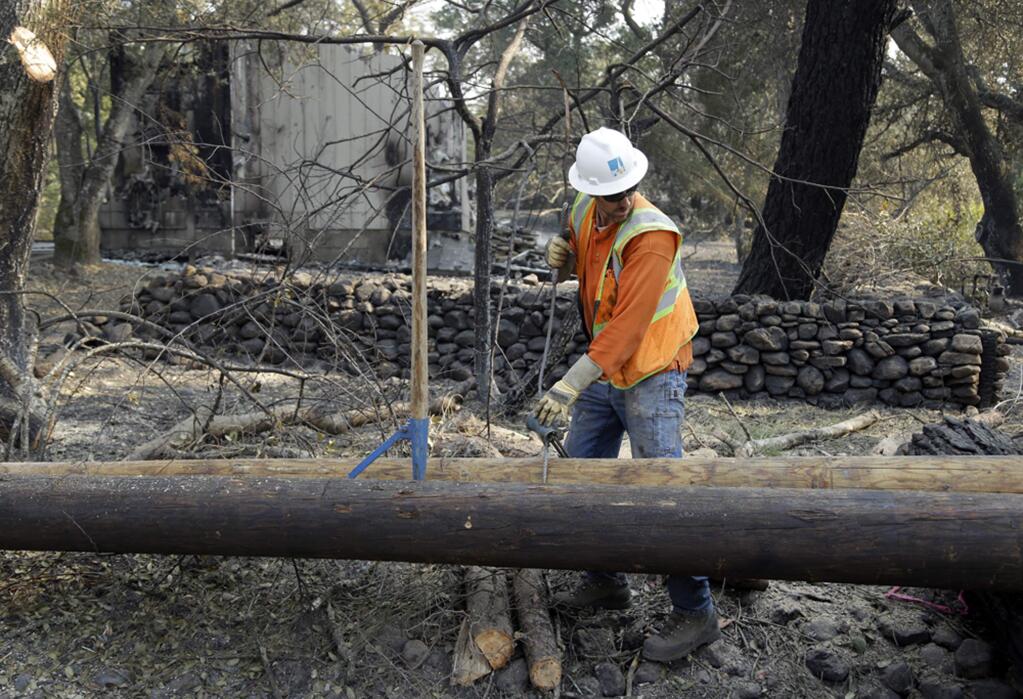 FILE - In this Oct. 18, 2017 file photo, a Pacific Gas & Electric worker replaces power poles destroyed by wildfires in Glen Ellen, Calif. California fire officials say sagging PG&E power lines that made contact ignited a blaze last year in California that killed four people and injured a firefighter. The California Department of Forestry and Fire Protection said Tuesday, Oct. 9, 2018 that strong winds caused the lines to come into contact and send molten material onto dry vegetation in Yuba County. It was one of several wildfires that swept through Northern California that month, killing 44 people. (AP Photo/Ben Margot, file)