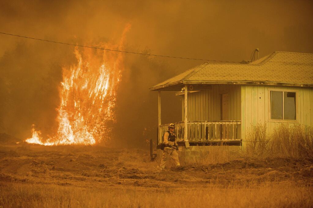 Flames rise behind a vacant house as a firefighter works to halt the Detwiler wildfire near Mariposa, Calif., on Wednesday, July 19, 2017. As wildfires rage throughout the western U.S., one California blaze in the rugged mountains outside of Yosemite National Park forced thousands of nearby residents to flee their homes. (AP Photo/Noah Berger)
