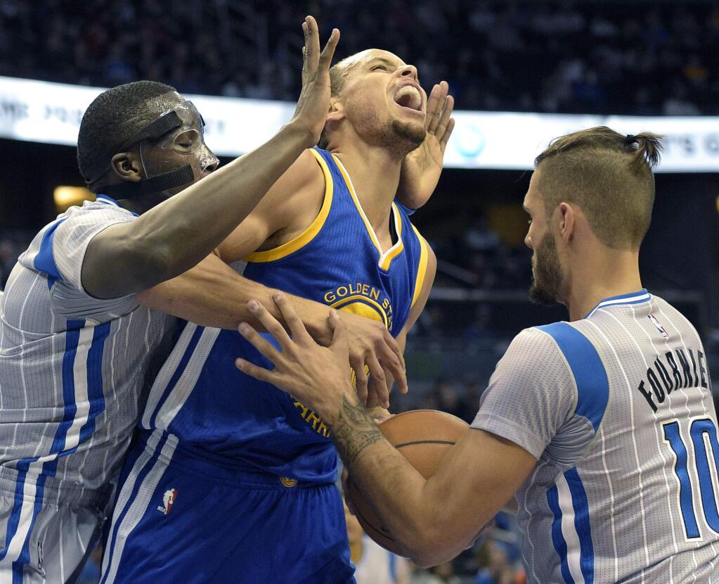 Golden State Warriors guard Stephen Curry, center, is fouled while going up for a shot between Orlando Magic guard Victor Oladipo, left, and guard Evan Fournier (10), of France, during the first half of an NBA basketball game in Orlando, Fla., Wednesday, Nov. 26, 2014. (AP Photo/Phelan M. Ebenhack)