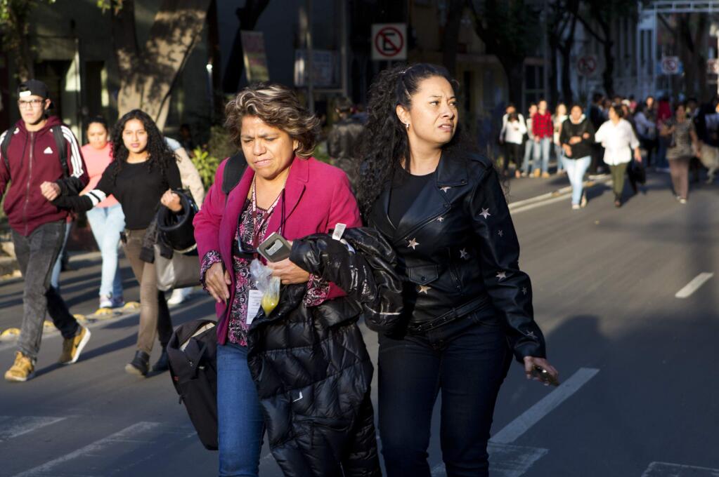 People walk down the center of a street in the Roma neighborhood after an earthquake shook Mexico City, Friday, Feb. 16, 2018. A powerful 7.2-magnitude earthquake has shaken south and central Mexico, causing people to flee buildings and office towers in the country's capital, and setting off quake alert systems.(AP Photo/Rebecca Blackwell)
