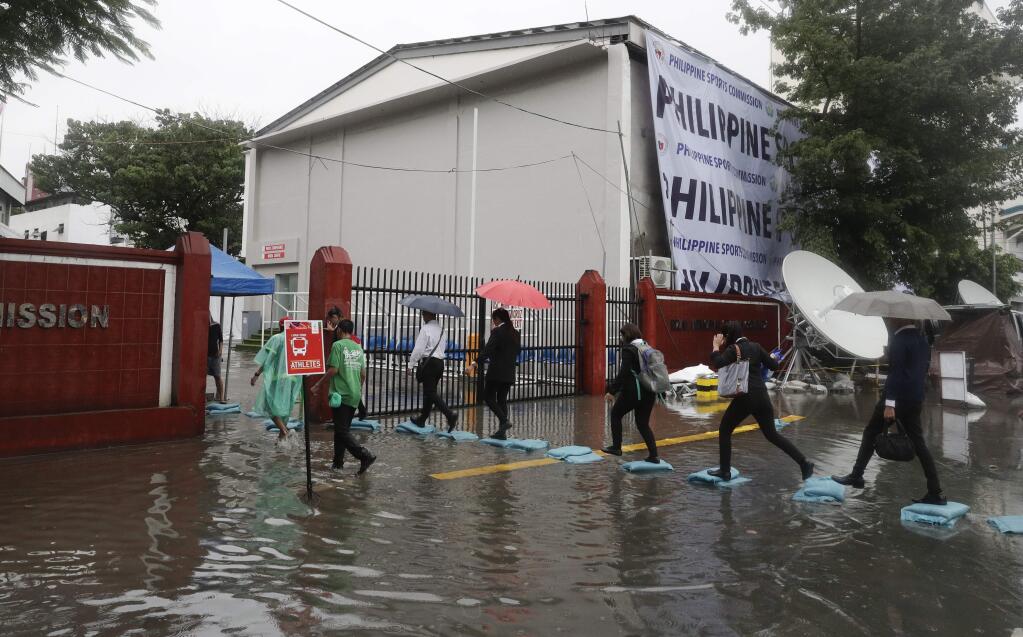 People walk over sand bags as they try to avoid a flooded portion of the entrance of the venues of the South East Asian games after rains from Typhoon Kammuri poured in Manila, Philippines on Tuesday, Dec. 3, 2019. A powerful typhoon was blowing across the Philippines on Tuesday after slamming ashore overnight in an eastern province, damaging houses and an airport and knocking out power after tens of thousands of people fled to safer ground. (AP Photo/Aaron Favila)