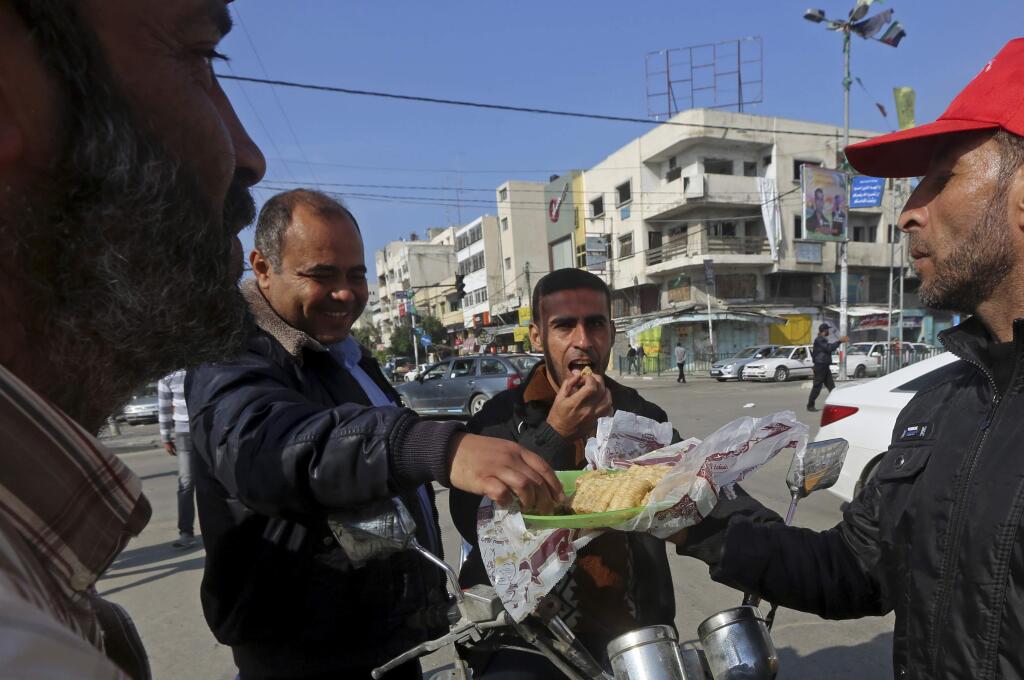 Palestinian supporters of the Popular Front for the Liberation of Palestine, a small militant group, offers sweets after hearing the news of a shooting attack inside a synagogue in Jerusalem, on a main road in Gaza City, northern Gaza Strip, Tuesday, Nov. 18, 2014. Two Palestinian cousins stormed a Jerusalem synagogue on Tuesday, attacking worshippers with meat cleavers and a gun during morning prayers and killing four people in the city's bloodiest attack in years. The attackers were killed in a shootout with police. (AP Photo/Adel Hana)