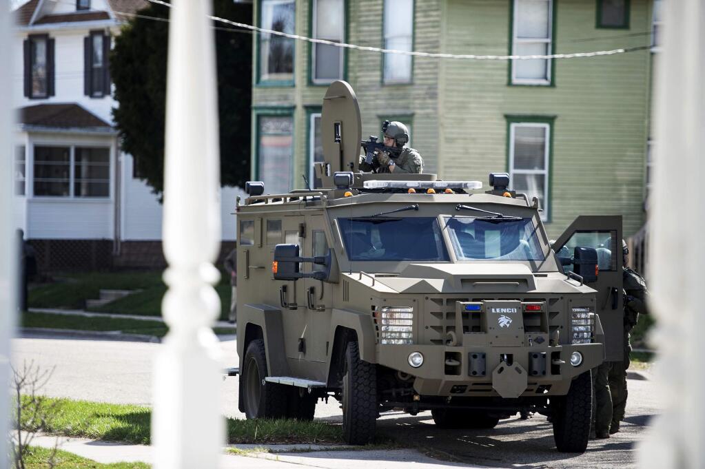 A man in tactical gear points a gun at a home on Eisenhower Avenue from an armored vehicle, Friday, April 7, 2017, in Janesville, Wis. (Angela Major/The Janesville Gazette via AP)