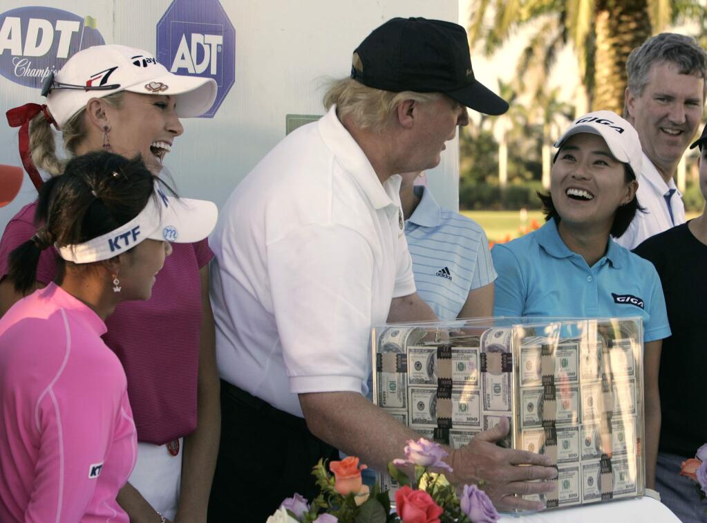 FILE - This Nov. 18, 2006 file photo shows Donald Trump, center, putting his hands on a box of money while posing for a photo with the eight golfers who qualified for the final round following the third round of the LPGA ADT Championship at the Trump International Golf Club in West Palm Beach, Fla. Also present, from left to right, are: Mi Hyun Kim, of South Korea, Natalie Gulbis and il Mi Chung, also of South Korea. The U.S. Women's Open will be played next week at a golf course in New Jersey owned by President Trump. The USGA awarded the site in 2012 and later came under pressure from women's groups and three Democratic U.S. senators to move the event because of Trump's comments about women and minorities. It's uncertain if the president will attend the tournament in Bedminster, New Jersey. (AP Photo/Lynne Sladky)