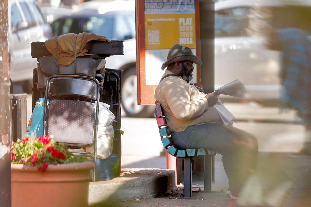 A homeless man known as Big Joe reads a newspaper with a large pile of his belongings, including several musical instruments, stacked in a planter behind him at the corner of 4th and D streets in Santa Rosa, California on Tuesday, October 11, 2016. (Alvin Jornada / The Press Democrat)