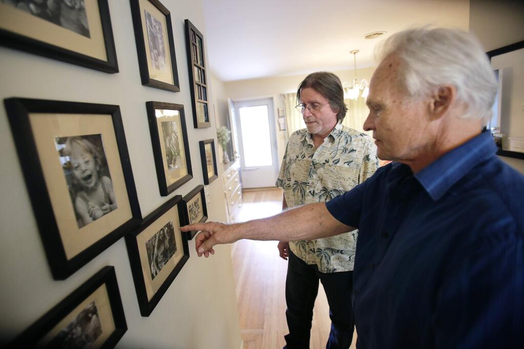 Mike Sullens, left, and Walter Rabideau look at old photos of their band, The Farm Band at Walter's home in Petaluma on Friday, August 6, 2014. (Conner Jay/The Press Democrat)