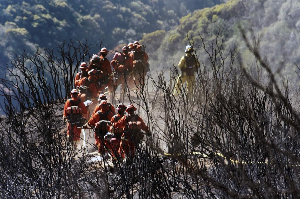 In this photo provided by the Santa Barbara County Fire Department, CAL FIRE Inmate Firefighting Hand Crew members hike through the charred landscape on their way to work east of Gibraltar Road above Montecito, Calif., Tuesday, Dec. 19, 2017. Officials estimate that the fire will grow to become the biggest in California history before full containment, expected by Jan. 7. (Mike Eliason/Santa Barbara County Fire Department via AP)