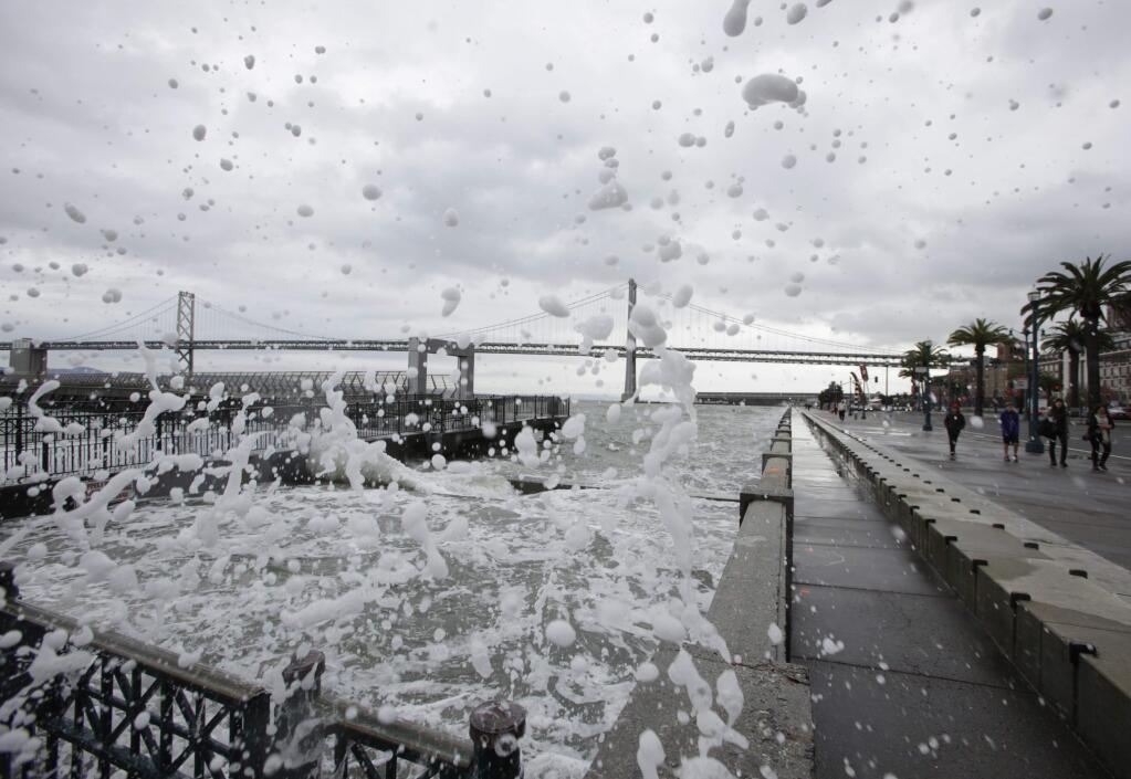 FILE - In this Dec. 20, 2010, file photo, waves crash against a seawall as people make their way along the Embarcadero in San Francisco. The Embarcadero made The National Trust for Historic Preservation's 2016 list of America's 11 Most Endangered Historic Places, an annual list that spotlights important examples of the nation's architectural and cultural heritage that are at risk of destruction or irreparable damage. (AP Photo/Eric Risberg, File)