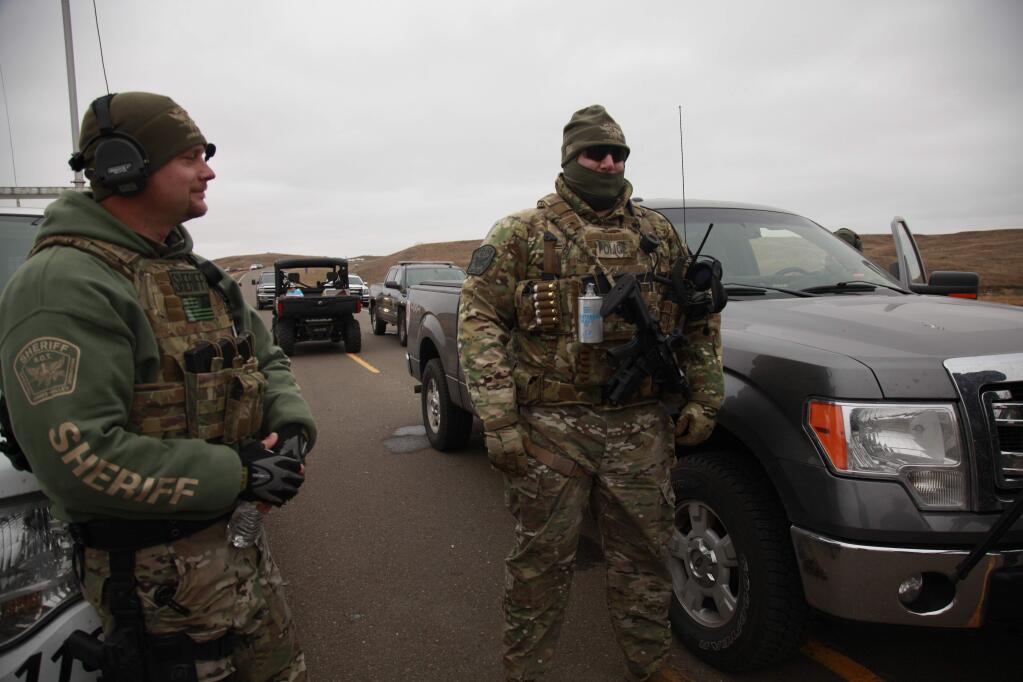 Two members of the Stutsman County SWAT team talk while deployed to watch protesters demonstrating against the Dakota Access Pipeline encroaching the water source near the Stand Rock Sioux Reservation, as they stand next to a police barricade on Highway 1806 in Cannon Ball, N.D., Sunday, Oct. 30, 2016. (AP Photo/John L. Mone)
