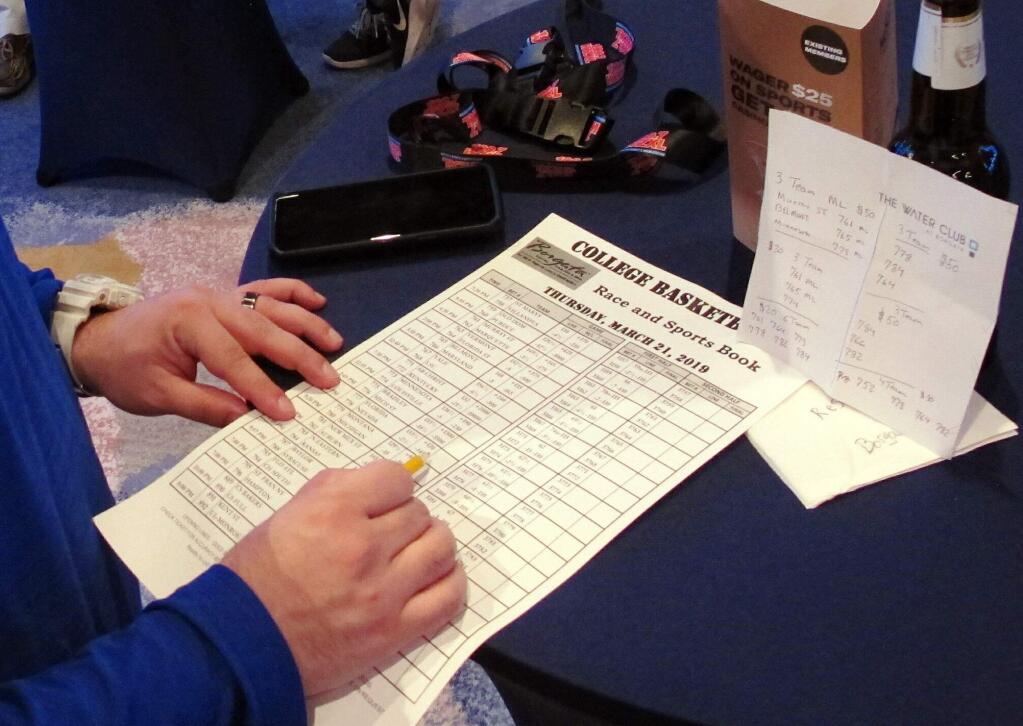 A gambler looks over a race and sportsbook sheet for the NCAA Tournament Thursday, March 21, 2019, at the Borgata casino in Atlantic City N.J. This is the first March Madness tournament since legal gambling expanded last year following a U.S. Supreme Court ruling involving a case brought by New Jersey. (AP Photo/Wayne Parry)