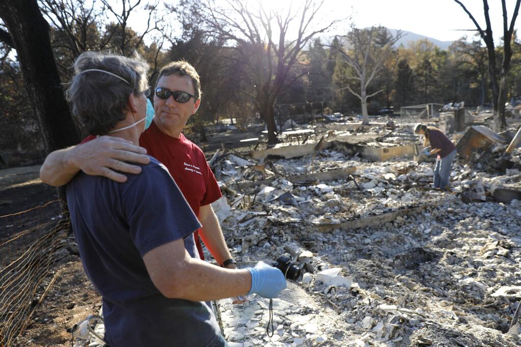 Homeowner Arthur Dawson, left, gets a hug from his neighbor Steve Lee as he and his wife Jill, right, dig through the rubble of their burned home on Warm Springs Rd on Sunday, October 22, 2017 in Glen Ellen, California . (BETH SCHLANKER/The Press Democrat)
