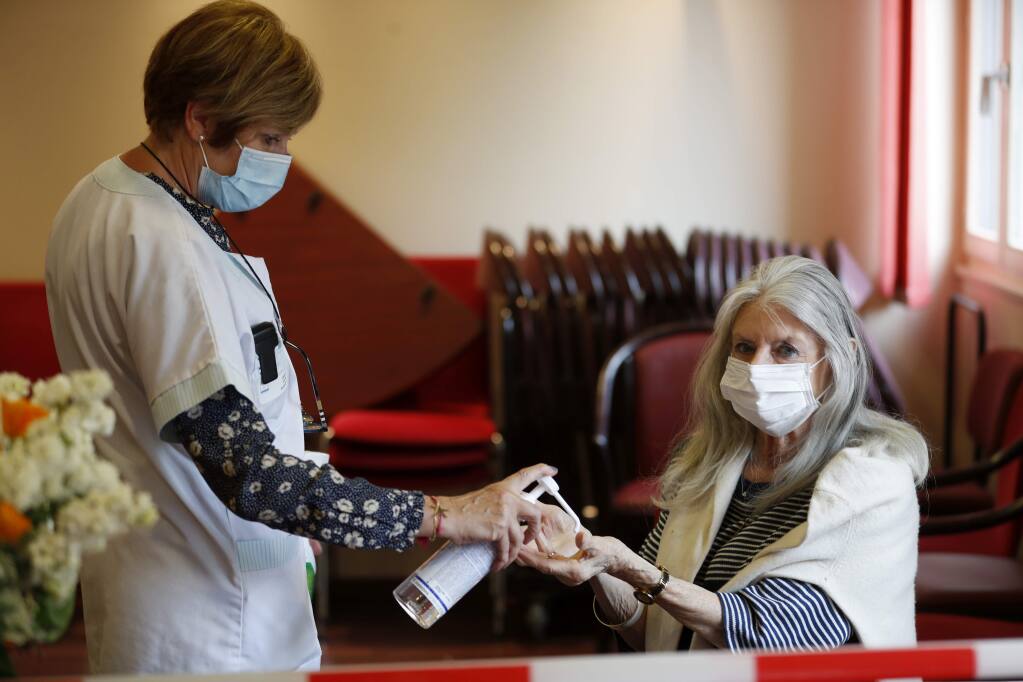 An employee sprays alcoholic gel on Josiane Cohen, right, before meeting her daughter Laetitia at the Kaysersberg nursing home, eastern France, Tuesday April 21, 2020. France banned all nursing home visits early in the pandemic, and many residents have been confined to their rooms for weeks, because the coronavirus has been especially dangerous for the elderly. France made an exception to its strict virus confinement measures to allow families to visit relatives in nursing homes since Monday. (AP Photo/Jean-Francois Badias)
