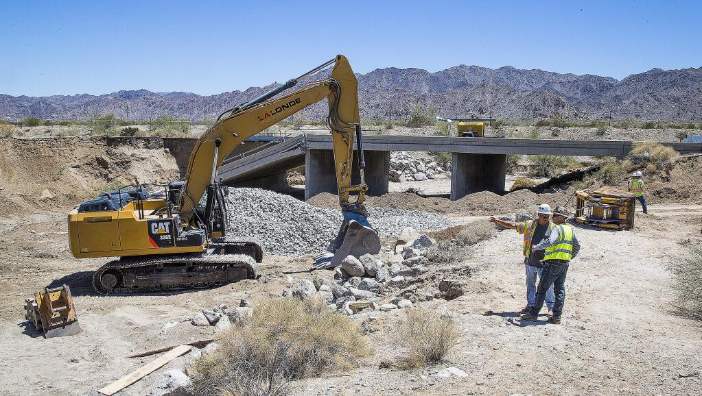 Construction workers stand near the collapsed elevated section of Interstate 10, Wednesday, July 22, 2015, near Desert Center, Calif. Crews continued worked to fortify the bridge that a surge of floodwater damaged with a goal to reopen the main route connecting Los Angeles and Phoenix by Friday. (Tom Tingle/The Arizona Republic via AP)