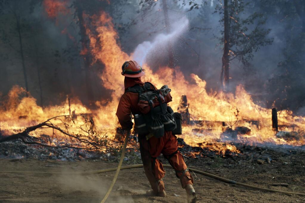 A firefighter with the Gabilan Camp crew hoses down hot spots during a controlled burn to fight the King Fire on Monday, Sept. 22, 2014, near Placerville, Calif. Crews scrambled Monday to extend control lines around a massive Northern California wildfire threatening thousands of homes as they braced for strong, erratic winds similar to when the blaze doubled in size a week ago. (AP Photo/Marcio Jose Sanchez)