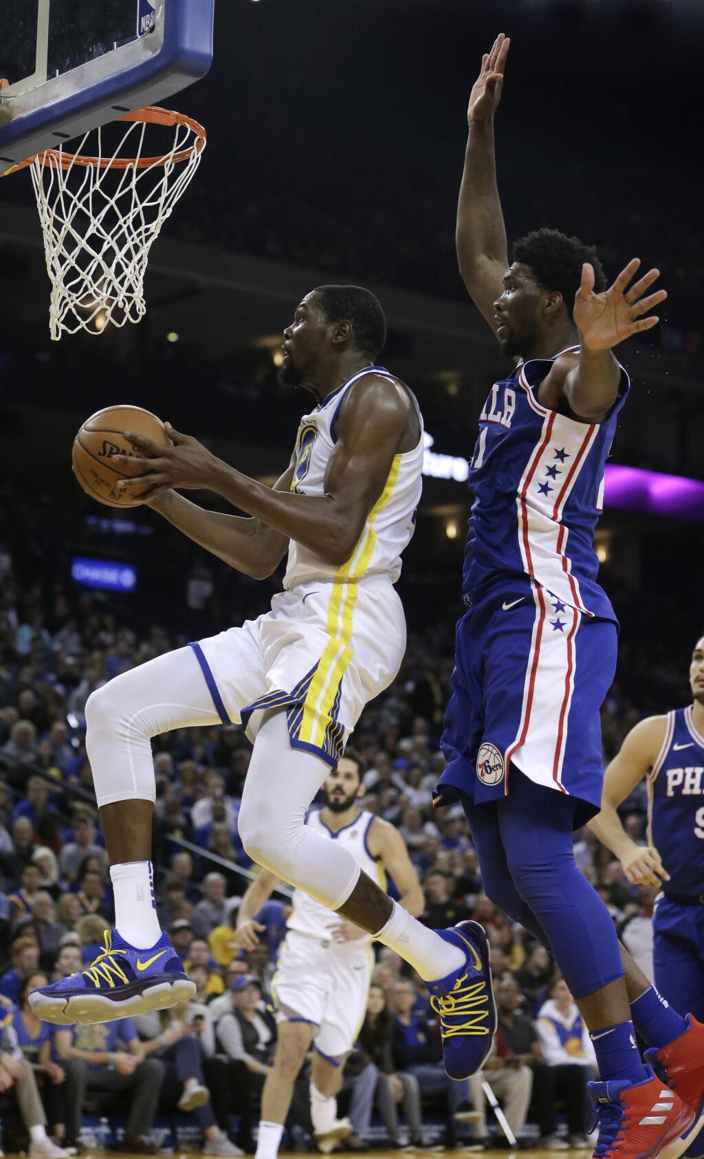 Golden State Warriors' Kevin Durant, left, lays up a shot past Philadelphia 76ers' Joel Embiid during the first half of an NBA basketball game Saturday, Nov. 11, 2017, in Oakland, Calif. (AP Photo/Ben Margot)