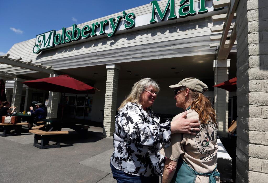 Regular customer Terrie King, left, of Windsor greets Molsberry's Market 'BBQ queen' Donna Lane who has worked at Molsberry's for 19 years, in the Larkfield Shopping Center, in Santa Rosa, California, on Friday, April 27, 2018. Shops around the Larkfield-Wikiup neighborhood are experiencing a slowdown in business during the aftermath of the Tubbs fire. (Alvin Jornada / The Press Democrat)