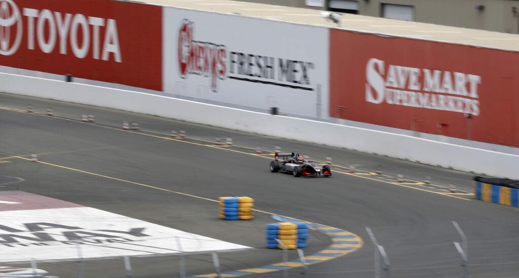A race car drives around the track past billboards that could be used by Sonoma-USA, to make a variety of bags from raceway materials, at Sonoma Raceway on Wednesday, May 25, 2016 in Sonoma, California . (BETH SCHLANKER/ The Press Democrat)