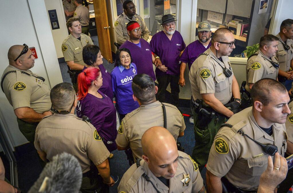 Labor leader Dolores Huerta, center, joins several other protesters in linking arms outside the Fresno County Board of Supervisors chambers shortly before being arrested Tuesday, Aug. 20, 2019, in Fresno, Calif. Huerta has been arrested along with several other union members during a protest to demand a raise for Fresno county home care workers. The Fresno Bee reports sheriff deputies put Huerta and the others in plastic handcuffs and removed them Tuesday from the entrance to the Board of Supervisors chambers, where supervisors were holding a closed meeting. (Craig Kohlruss/The Fresno Bee via AP)