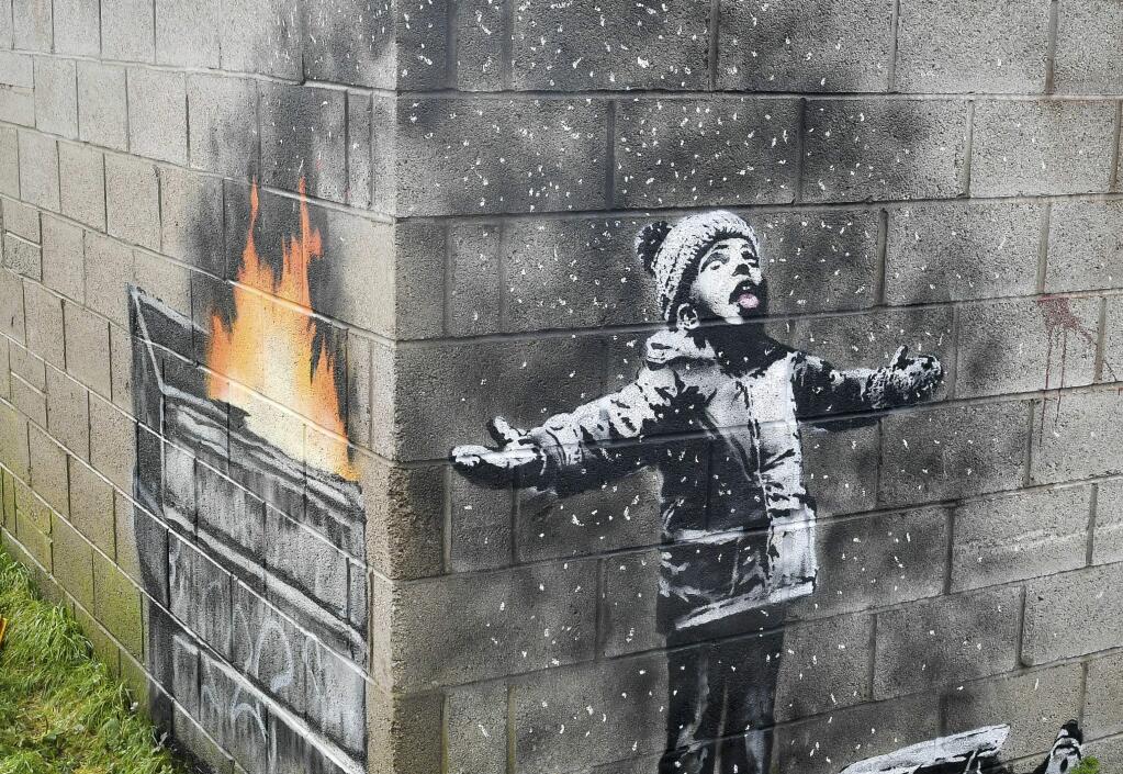 FILE - In this file photo dated Dec, 20, 2018, showing an artwork by Banksy on the side of a garage depicts a child dressed for snow playing in the falling ash and smoke from a skip fire, in Port Talbot, Wales. The artwork has been sold to an Essex art dealer for a 'six-figure sum', although the mural will stay in its current location for about two-years, it is revealed Friday Jan. 18, 2019. (Ben Birchall/PA FILE via AP)