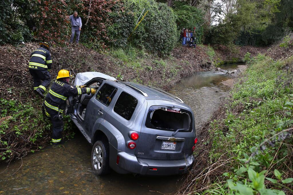 Geyserville firefighter Nathaniel Miller places debris into a vehicle that crashed into a creek, at Dry Creek and Dutcher Creek roads, following a high-speed chase near Cloverdale on Wednesday, March 22, 2017. (Christopher Chung/ The Press Democrat)