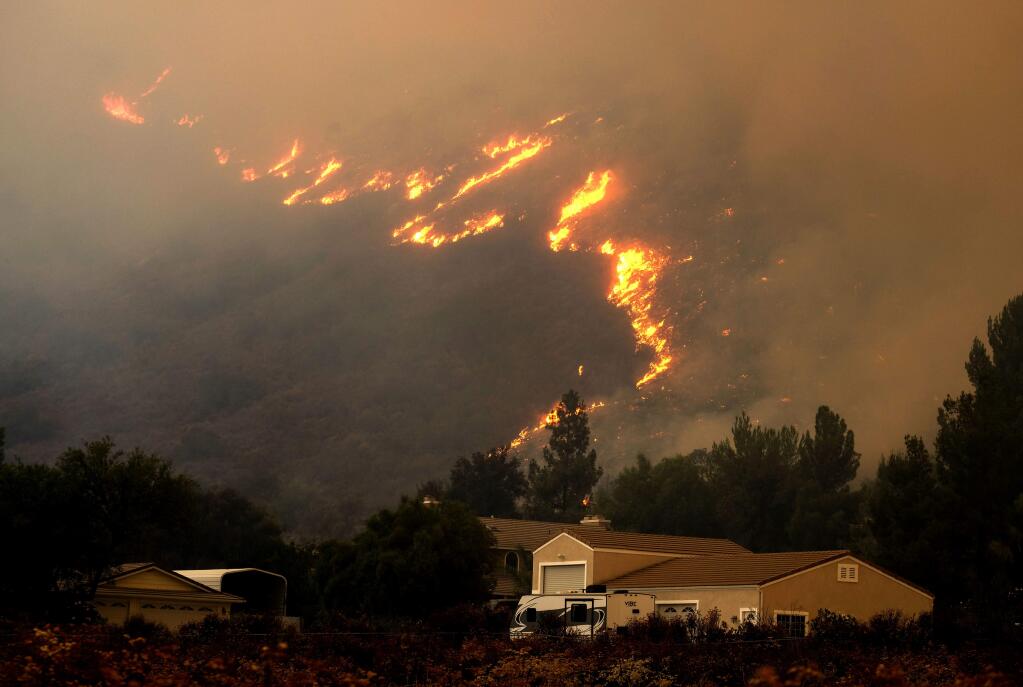 FILE- In this Aug. 9, 2018, file photo a wildfire in the Cleveland National Forest at a hillside near homes in Lake Elsinore, Calif. California homeowners may find themselves facing insurance issues even if they were not directly hit by this year's blazes. The California Department of Insurance warned in January that the increasing number and severity of wildfires in the state were making it more difficult for homeowners to find and hold on to insurance. And now they say that recent massive fires may make the problem more acute. (AP Photo/Ringo H.W. Chiu, File)